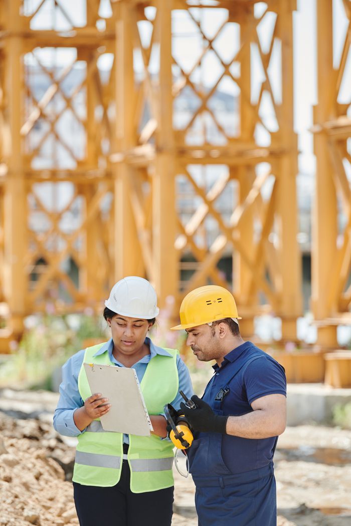 Male and female construction workers discussing plans at an outdoor construction site.